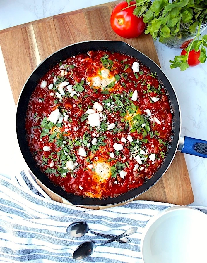 Gorgeous deep red spicy Shakshuka with Chorizo Sausage served in a skillet and topped with feta cheese, fresh parsley and delicately cooked eggs.